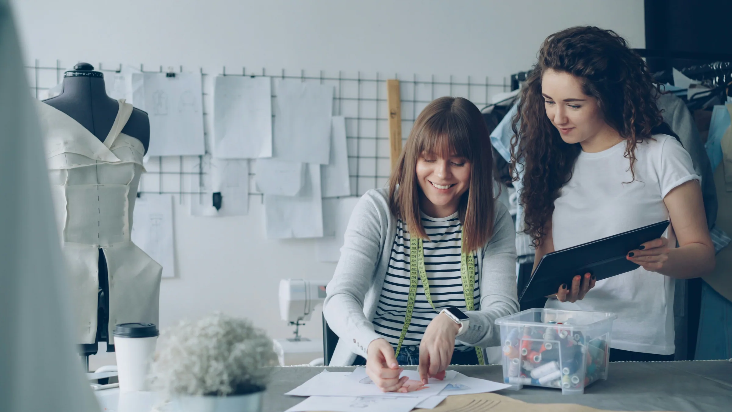 Two fashion designers reviewing garment drawings and a tablet together
